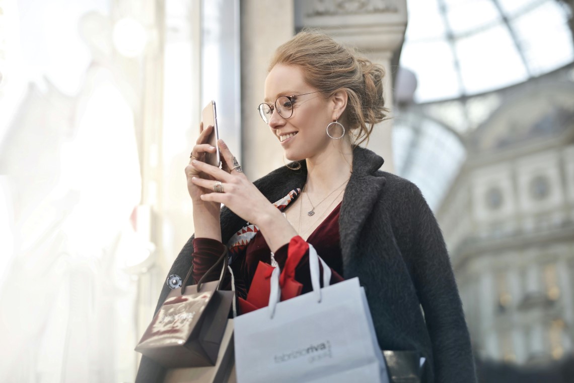 Woman Holding Shopping Bags Checking Her Credit Card Balance On Her Phone Woman Holding Shopping Bags Checking Her Credit Card Balance On Her Phone